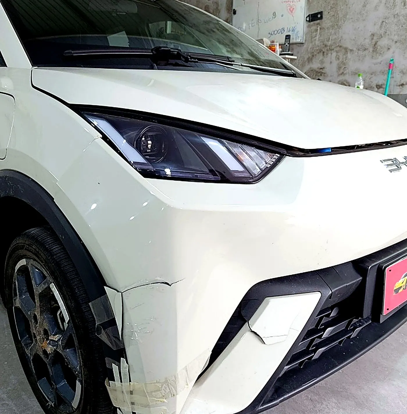 BYD branco com o parachoque dianteiro rachado e preso com fita, antes do reparo